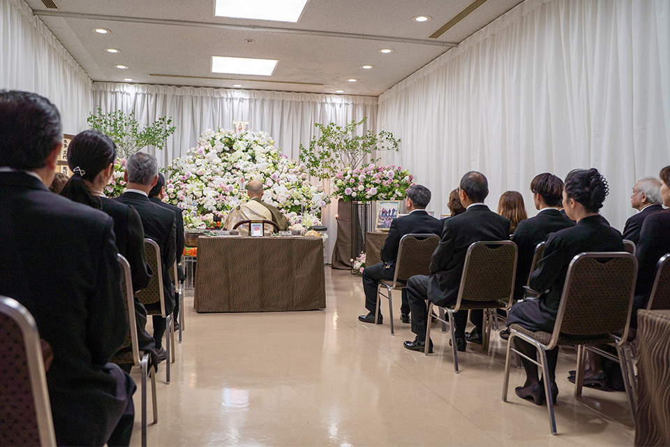 葬儀撮影サービス｜燈が祭壇前で葬儀撮影を行う参列者と白い花の祭壇