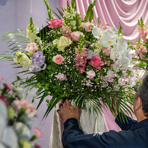 葬儀撮影サービス|燈が祭壇前に飾る白とピンクの弔花アレンジを調整している