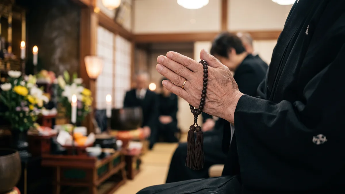 数珠を手に静かに合掌する参列者の手元、葬儀での祈りの場面