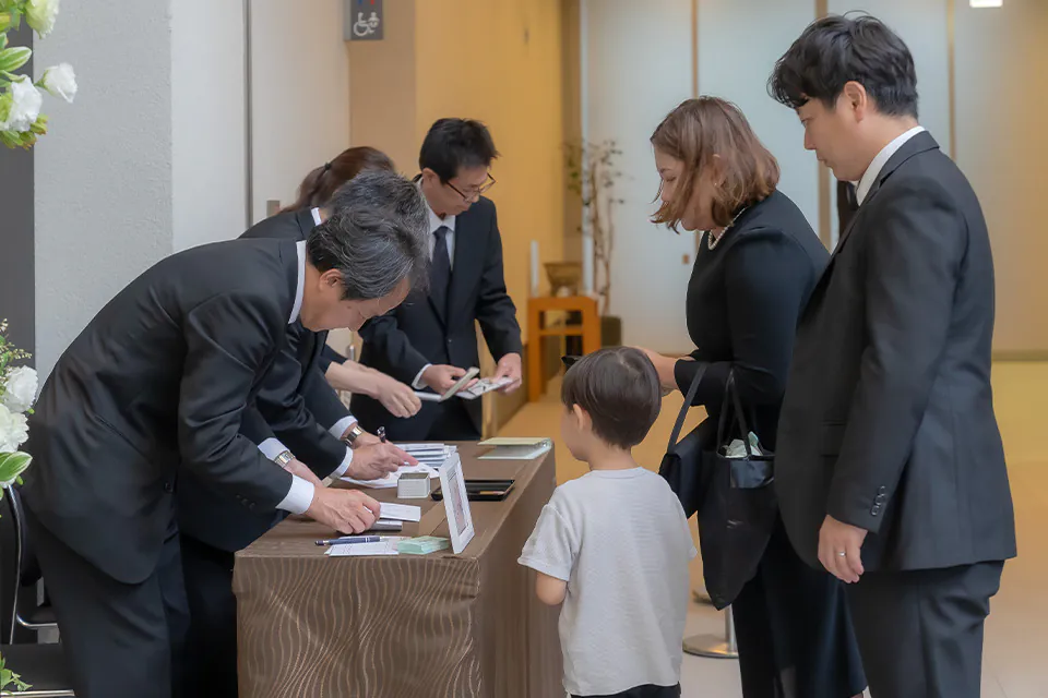 受付で葬儀撮影の申込を家族が行う様子と葬儀撮影サービス｜燈の案内案内冊子