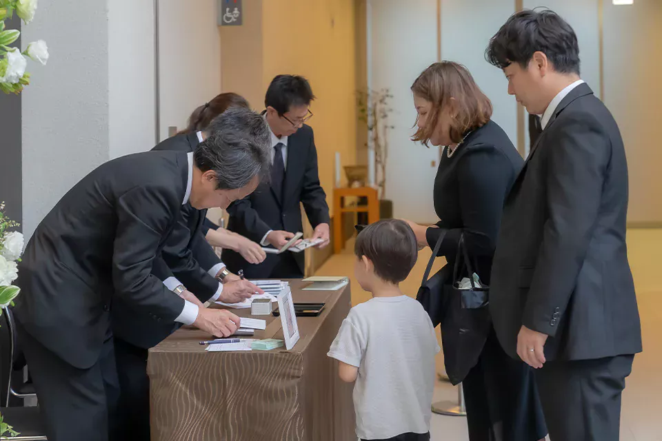 受付で葬儀撮影の申込を家族が行う様子と葬儀撮影サービス|燈の案内案内冊子